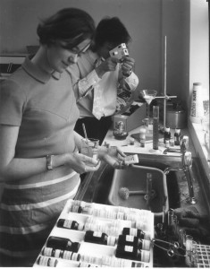 Science in the home. The man is using one of the 8,000 tiny, cheap, lightweight, microscopes designed by Dr John McArthur and sent out by the OU in 1971. Simple and robust (there was no delicate rack and pinion system) they were used to help create a new 'public'.